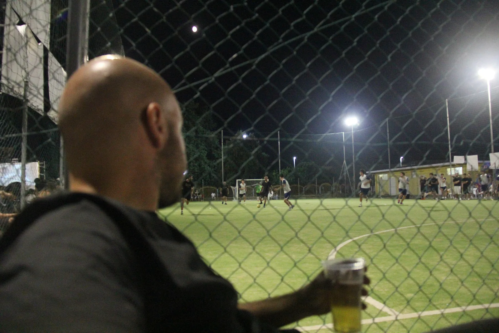 Uno spettatore osserva una partita di calcio a 5 attraverso la recinzione del campo.