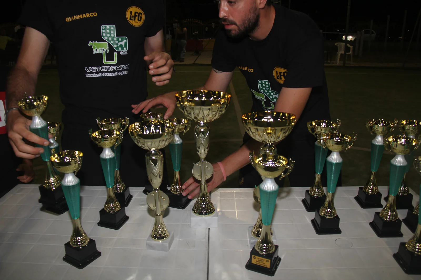 Due componenti dello staff preparano i trofei su un tavolo a bordo campo.